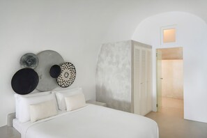 A bedroom with a bed, a wardrobe, and a wall with decorative plates. - Executive  Suite with Caldera View & Hot Tub (Santorini)