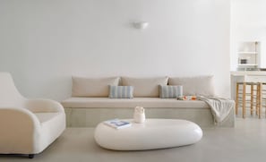 A minimalist living room with a sofa, a round ottoman, and a side table with a book and a vase. - Executive  Suite with Caldera View & Hot Tub (Santorini)