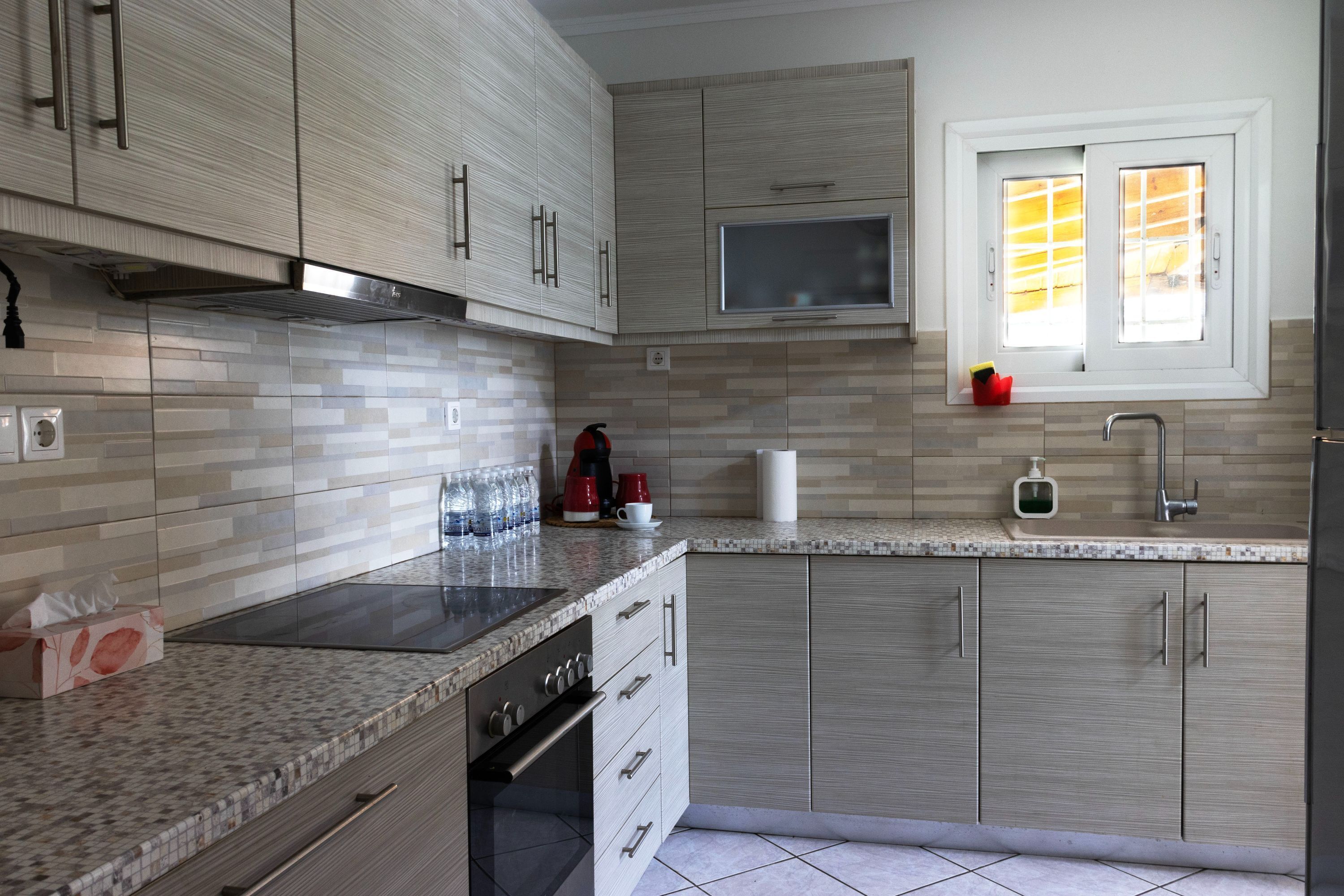 A modern kitchen with a built-in oven, stainless steel cabinets, a window with blinds, and a countertop with various items.