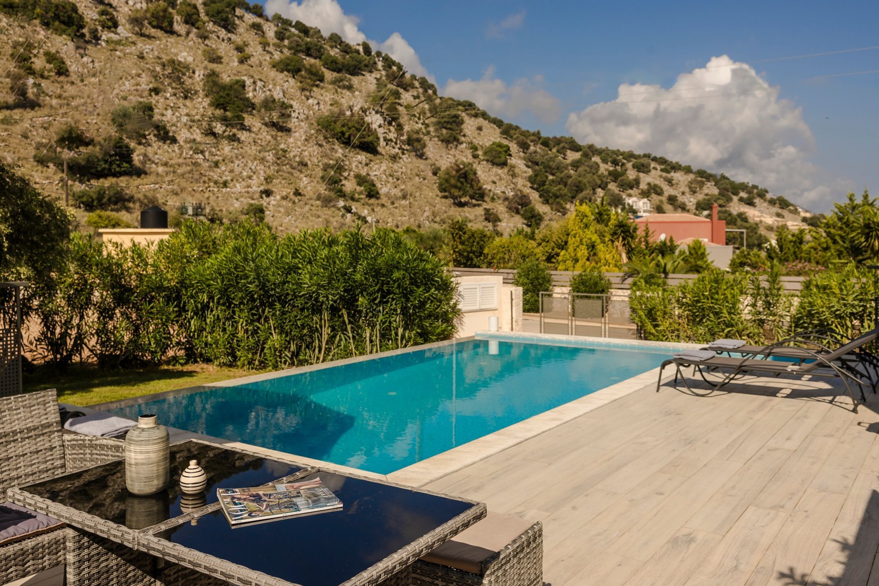 Une piscine avec une terrasse en bois, des meubles en osier et une vue sur un paysage montagneux.