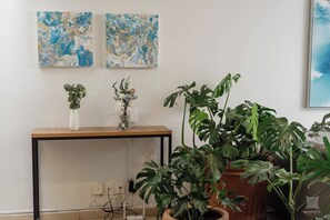 Une pièce comprenant une console en bois, deux tableaux accrochés au mur, une plante en pot et une grande plante monstera en pot.