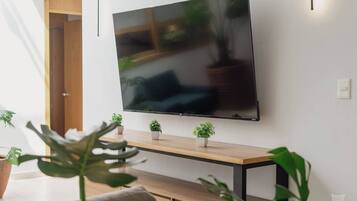 Een moderne woonkamer met een flatscreen televisie aan de muur, een houten salontafel en diverse potplanten.