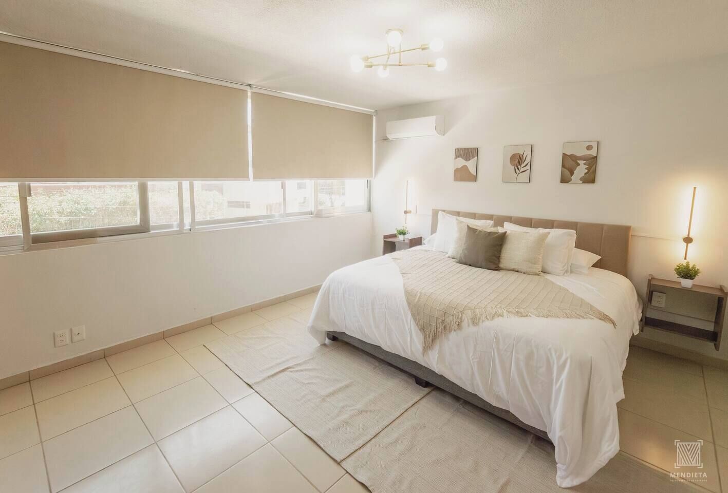 A spacious bedroom with a large bed, a bedside table with a lamp, and a window with blinds.