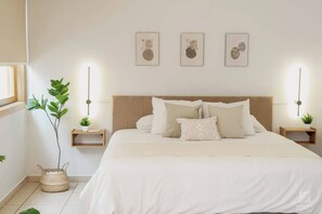Une chambre à coucher bien rangée, avec un grand lit, deux tables de chevet et trois tableaux accrochés au mur.