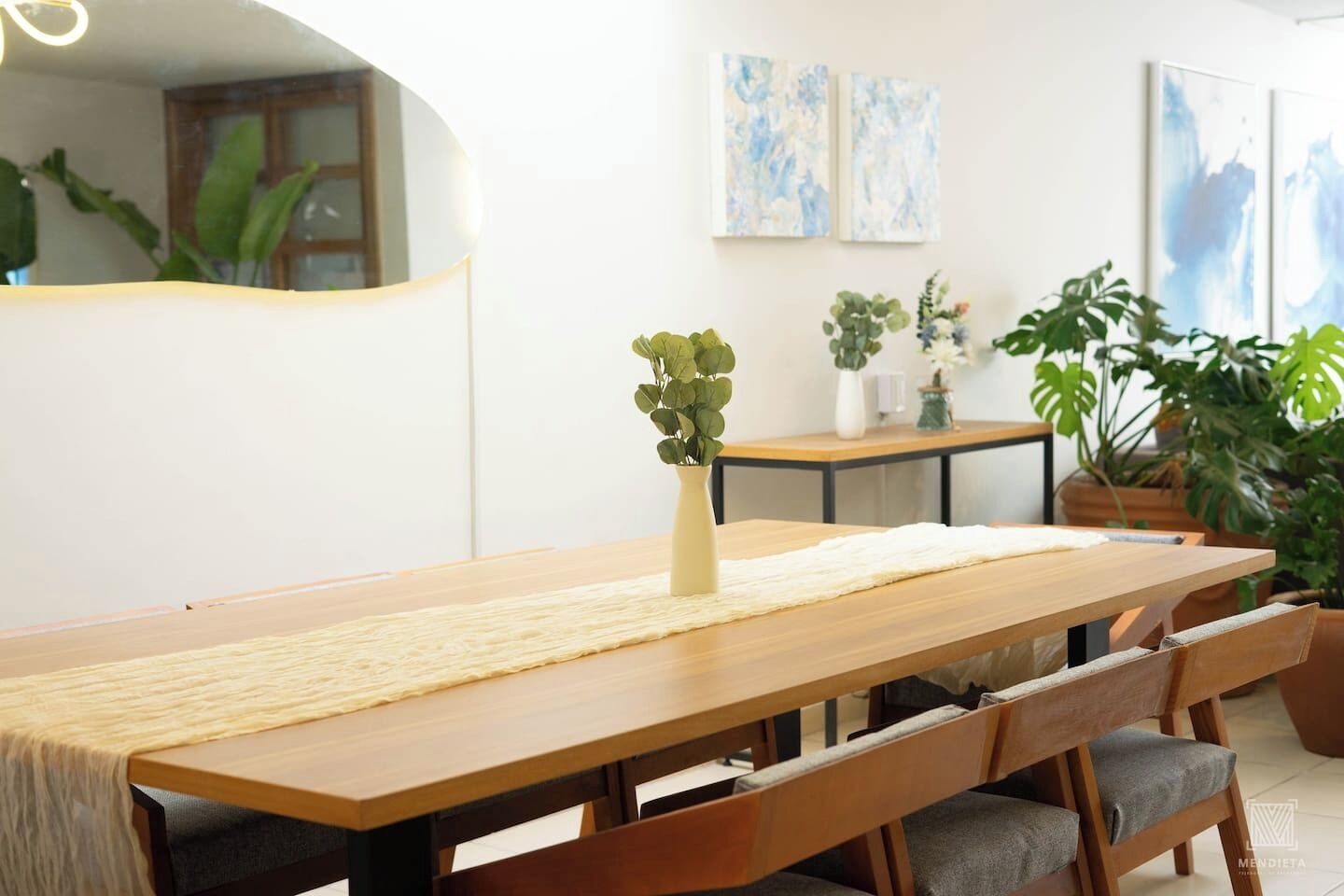 A dining area with a wooden table, cushioned chairs, and a vase with greenery.