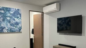 Un dormitorio con cama, televisión, aire acondicionado y un cuadro en la pared.