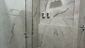 Ducha con azulejos de mármol, puerta de cristal y dos dispensadores de jabón.