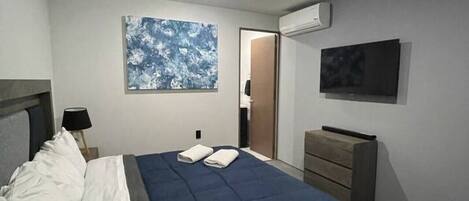 A modern bedroom with a bed, a nightstand, a dresser, a wall-mounted TV, and an air conditioning unit.