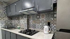 Una cocina con armarios oscuros, una estufa a gas, un refrigerador de acero inoxidable y azulejos decorativos en la pared.