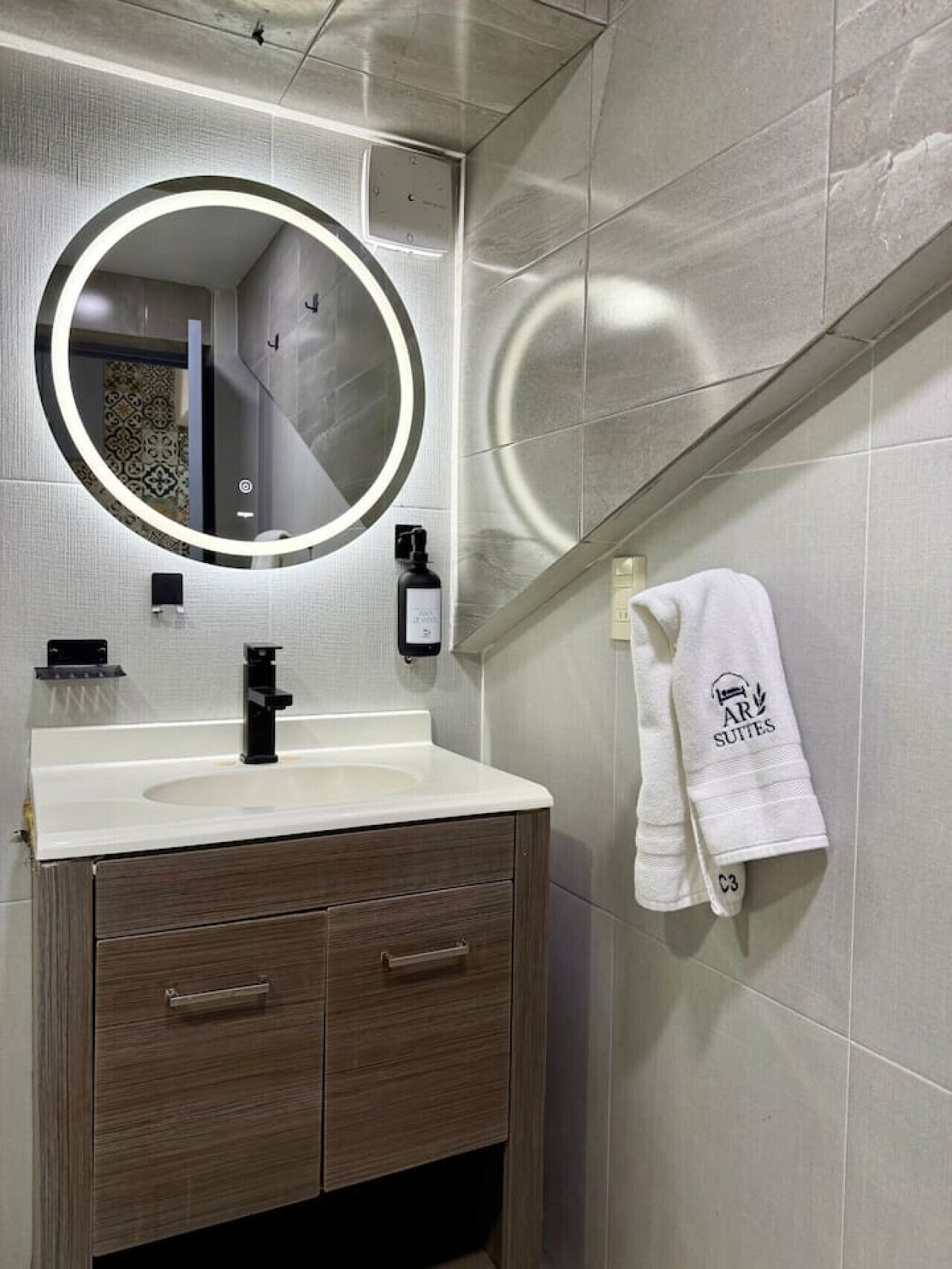 Un baño moderno con un espejo redondo, un lavamanos blanco y un perchero para toallas.