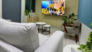 Moderni olohuone, jossa on sohva, pieni pöytä, tuoli ja seinälle asennettu taulutelevisio.