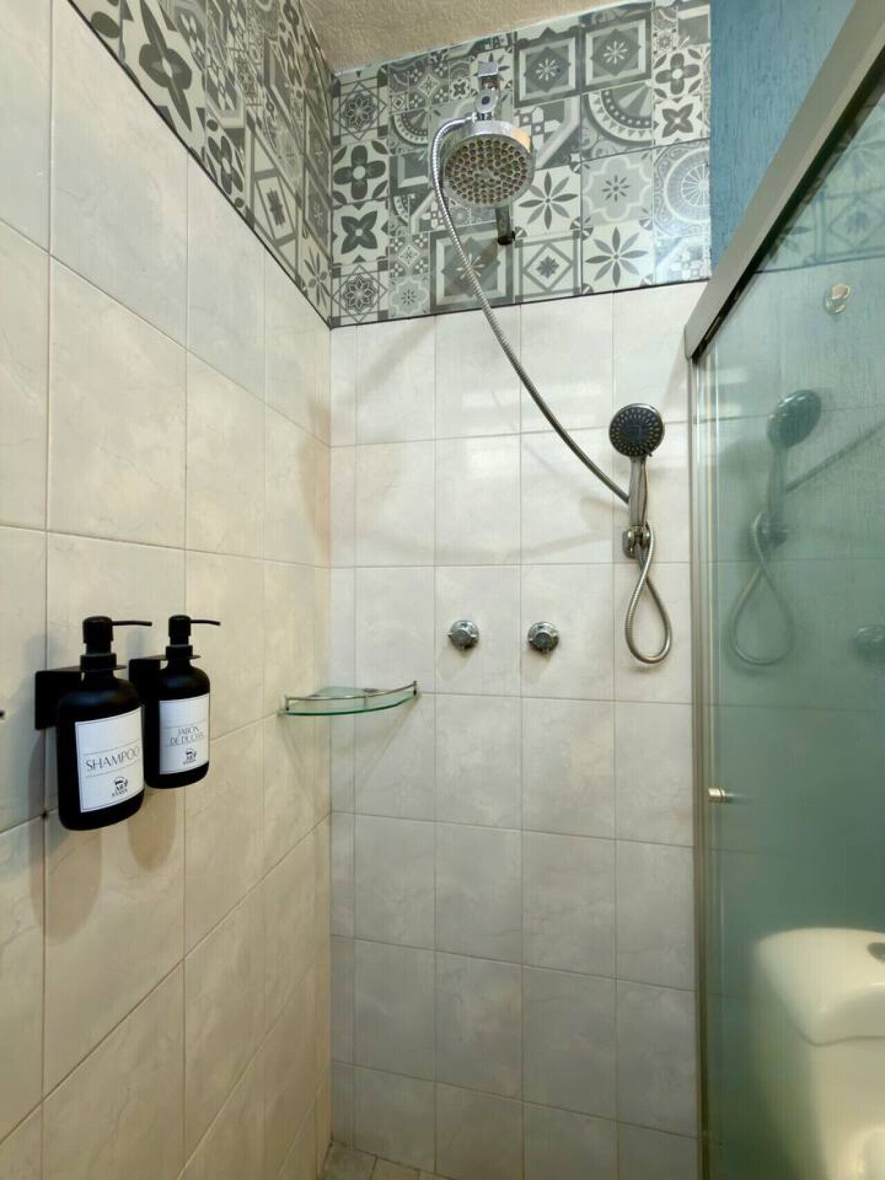 A shower area with a glass door, tiled walls, and two shampoo bottles on a wall-mounted holder.