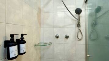 A shower area with a glass door, tiled walls, and two shampoo bottles on a wall-mounted holder.