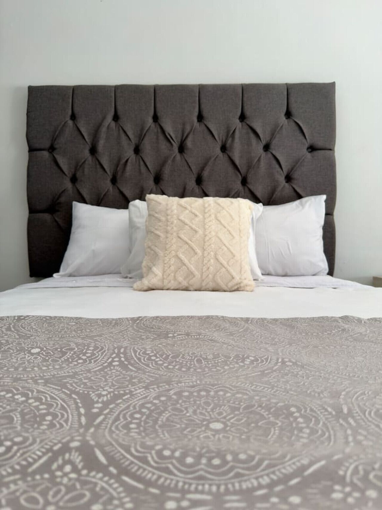 Een bed met een gestoffeerd hoofdbord, twee witte kussens en een beddekleed met een patroon.