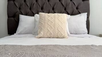 Een bed met een gestoffeerd hoofdbord, twee witte kussens en een beddekleed met een patroon.