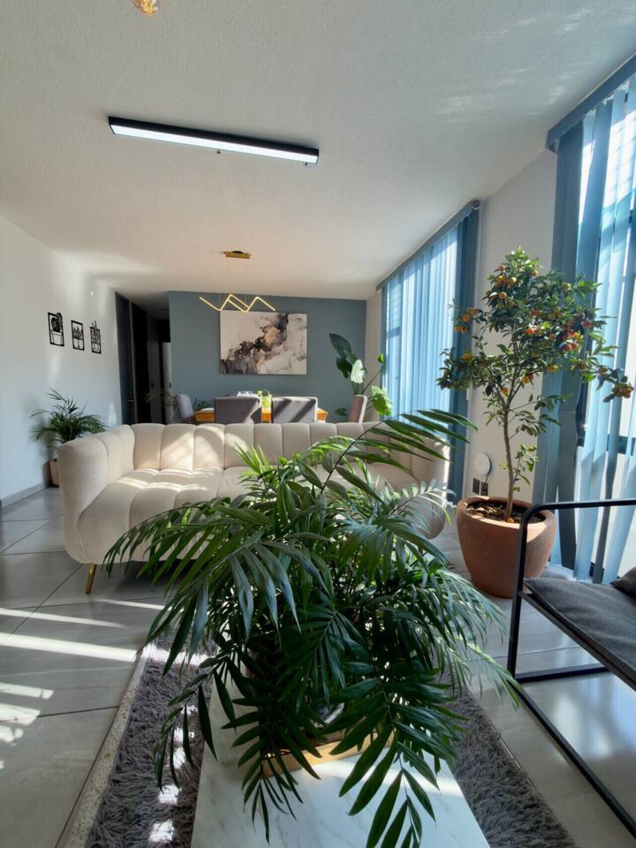 A modern living room with a sofa, a large potted plant, and a painting on the wall.