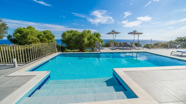 Una piscina rettangolare con acqua cristallina e blu, circondata da un bordo piastrellato e una recinzione in metallo.