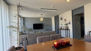 A modern dining area with a wooden table, grey upholstered chairs, a potted plant, and a ceiling light fixture. - AR Suites 4: La Calzada (Zamora de Hidalgo)
