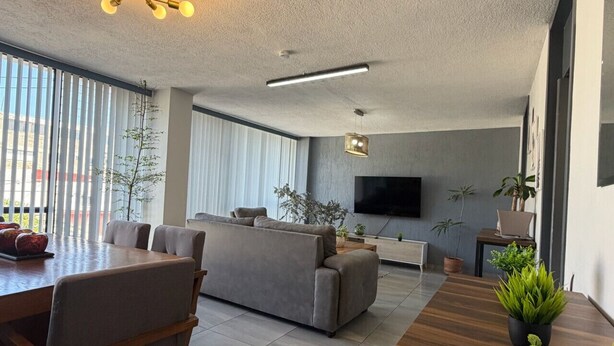 A modern living room with a sofa, dining table, and chairs, a flat-screen TV, and potted plants. - AR Suites 4: La Calzada (Zamora de Hidalgo)