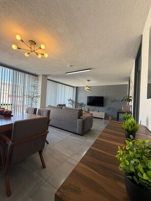 Un salon moderne comprenant un canapé, une table à manger et des chaises, un téléviseur à écran plat et des plantes en pot.