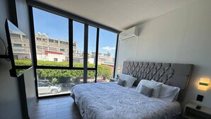 Ein Schlafzimmer mit großem Fenster, einem Bett mit gebogenem Kopfteil und einem Nachttisch mit Lampe.
