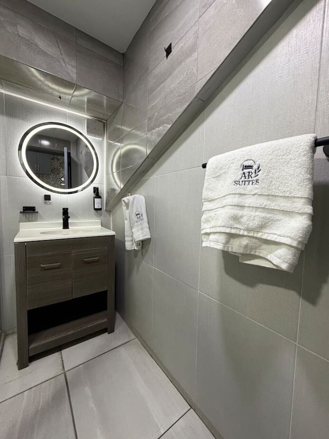 A modern bathroom with a vanity, a mirror with a light, and a towel rack with a towel.