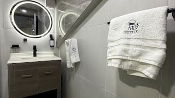 A modern bathroom with a vanity, a mirror with a light, and a towel rack with a towel.
