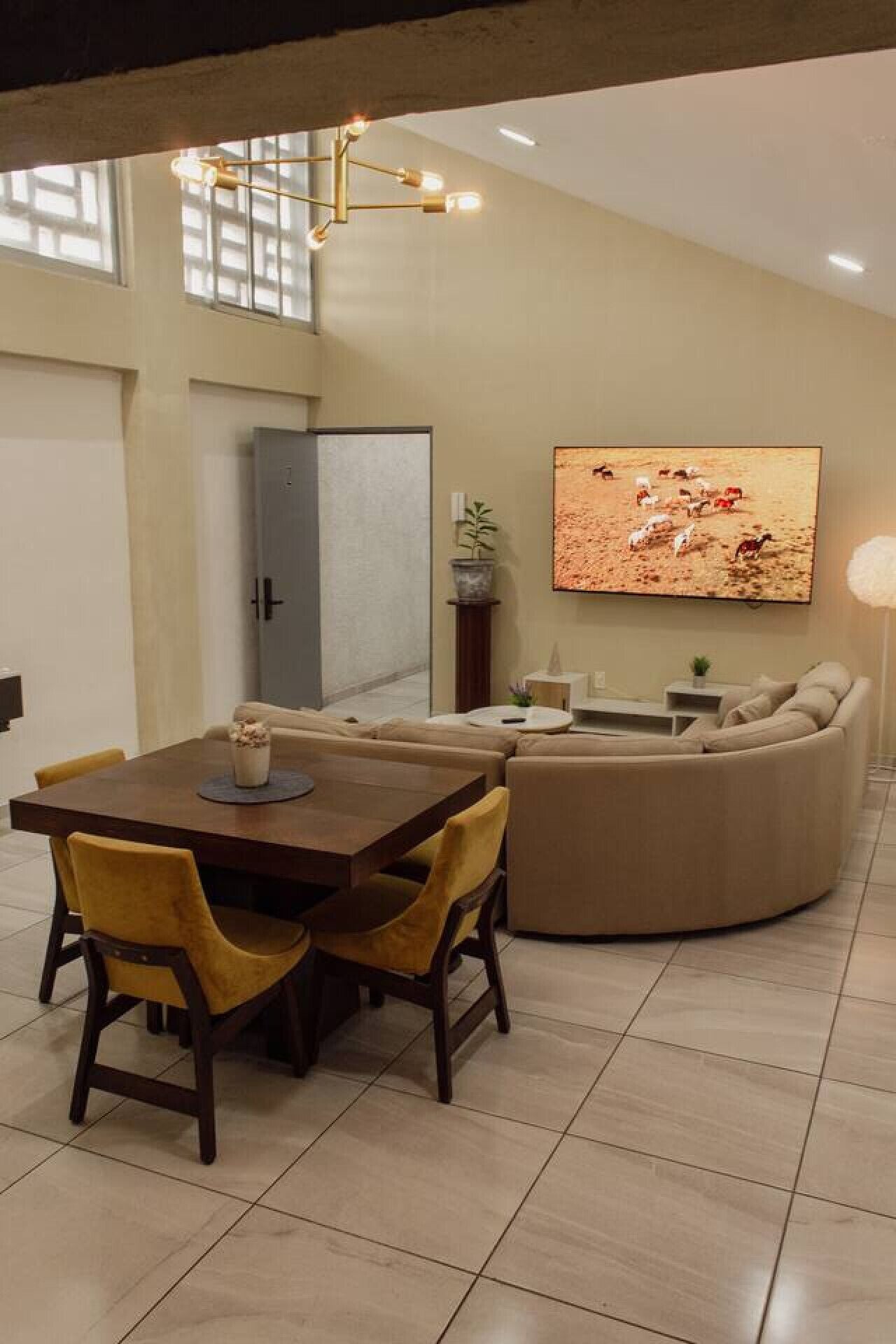 A modern living room with a dining area, featuring a large flat-screen TV, a sofa, and a dining table with chairs.