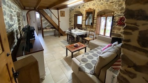 A rustic interior with a stone wall, wooden beams, a dining area, and a sofa. - Villa Fragk in Nipiditos village (Arkalochori)
