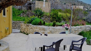An outdoor dining area with a table and chairs, surrounded by stone walls and greenery. - Villa Fragk in Nipiditos village (Arkalochori)