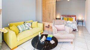 A modern living room with a yellow sofa, a pink sofa, a black coffee table, and a bed with a wooden headboard. - George's House in City center (Iraklio)