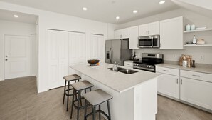 A modern kitchen with white cabinetry, a central island with stools, stainless steel appliances, and a built-in microwave. - 2025 Newly Constructed 3-Bedroom Townhome in Lovely North Fort Myers. (North Fort Myers)