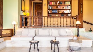 A cozy living room with a white sofa, two small tables, a bookshelf, and a staircase with a wooden railing. - La Belle Villa - Family Retreat & Magnificent View (Zakinthos)