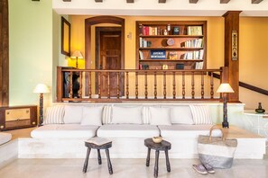 A cozy living room with a white sofa, two small tables, a bookshelf, and a staircase with a wooden railing. - La Belle Villa - Family Retreat & Magnificent View (Zakinthos)
