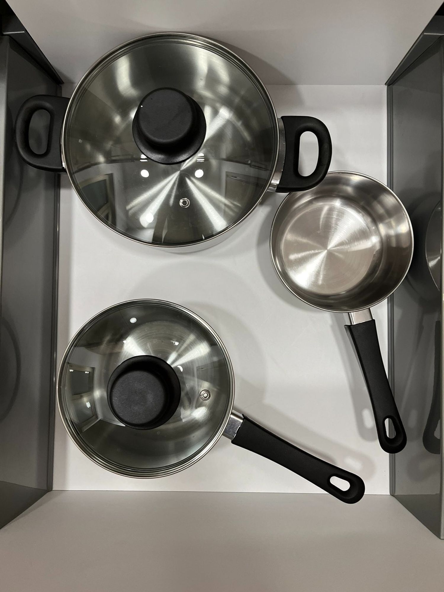 Una cucina con tre pentole e padelle in acciaio inossidabile su un piano di lavoro bianco.