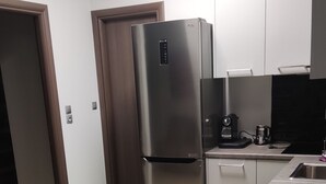 A modern kitchen with a stainless steel refrigerator, a coffee maker, and a sink. There is a dining table with black placemats and a teal mug. - Praxitelous Modern Suite by Athens Urban Retreat (Athina)