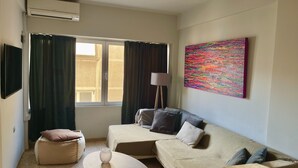 A living room with a sofa, a small table, a bean bag, a floor lamp, and a colorful abstract painting on the wall. - Praxitelous Modern Suite by Athens Urban Retreat (Athina)