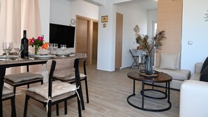 Uma sala de estar moderna com área de jantar, apresentando uma mesa de madeira para quatro pessoas, um sofá e uma mesa de centro.