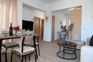 Ein modernes Wohnzimmer mit Essbereich, ausgestattet mit einem Holztisch für vier Personen, einer Couch und einem Couchtisch.