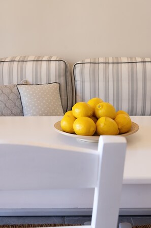 A white sofa with striped cushions and a bowl of lemons on a white table.
