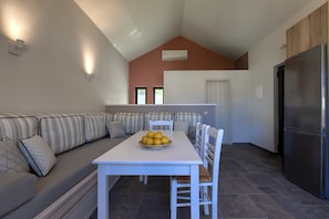A modern kitchen with a dining area, featuring a white table, striped sofa, and a stainless steel refrigerator.
