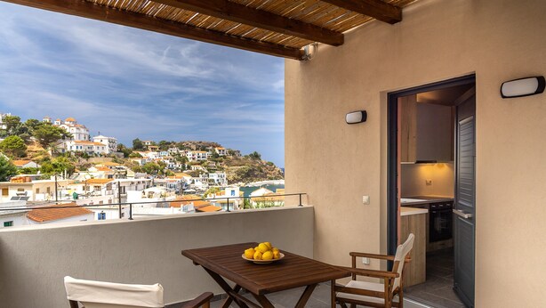 En balkon med et træbord og stole, en skål med citroner og udsigt til en by på en bakke.
