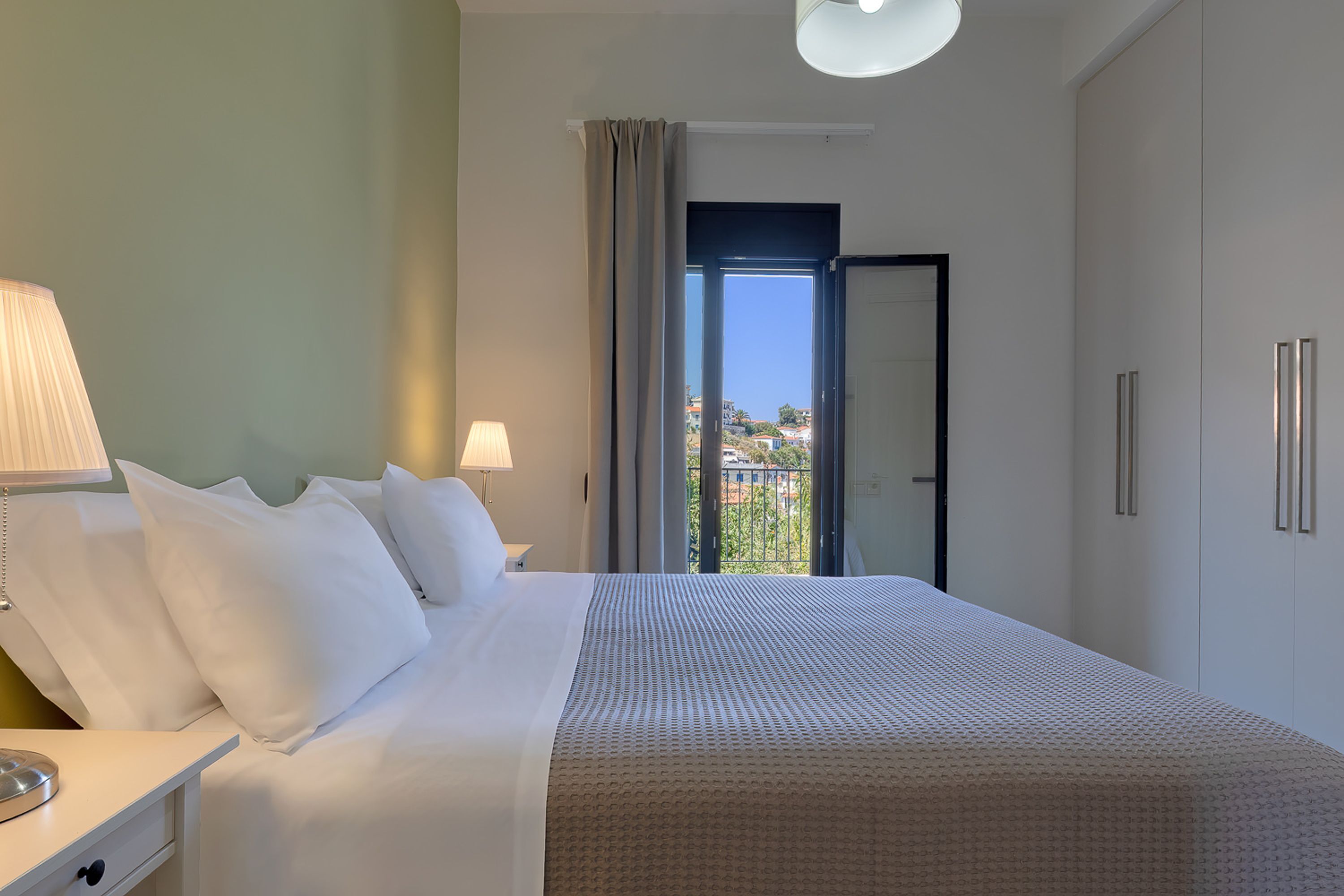Een hotelkamer met een bed, nachtlampjes, een nachtkastje, een kledingkast en uitzicht door een raam.