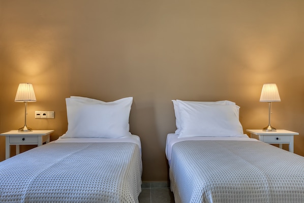 A hotel room with two beds, each with a white bedspread and matching pillows, flanked by nightstands with lamps.