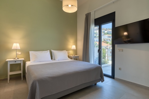 A bedroom with a bed, two bedside tables with lamps, a TV mounted on the wall, and a sliding glass door leading to an outdoor area.
