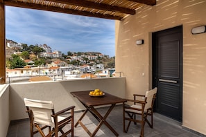 A balcony with a table and chairs, a door, and a view of a hillside town.