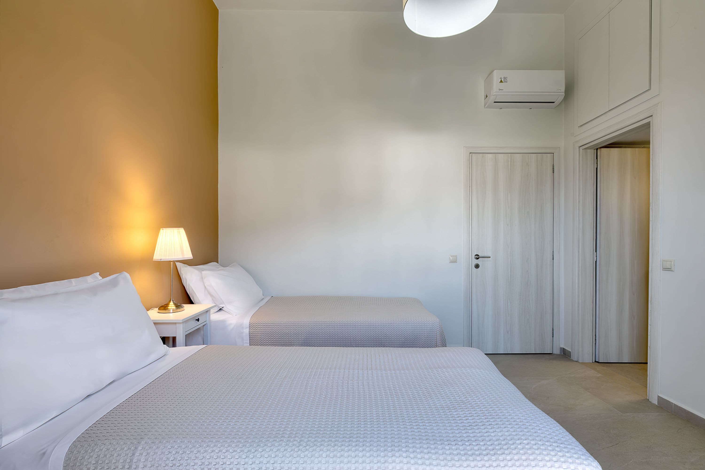 Ein Schlafzimmer mit zwei Betten, einem Nachttisch mit Lampe, einem Kleiderschrank und einer Klimaanlage.