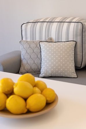 A sofa with striped cushions and a bowl of lemons on a table. - Lemonia Suites in Ikaria 4 (Kampos)