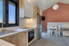 A modern kitchen with a large window, built-in oven, and a dining area with a table and chairs. - Lemonia Suites in Ikaria 4 (Kampos)
