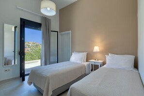 A hotel room with two beds, a bedside table with a lamp, a mirror, and a view of a hillside through an open door.